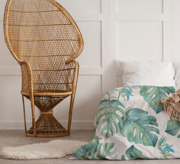 Tropical monstera palm leaf duvet in a white bedroom with neutral throw and whicker chair.