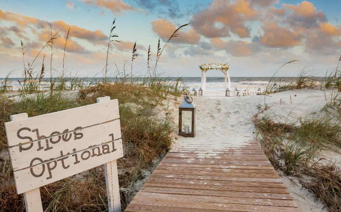 Seaside wedding ideas features a "Shoes Optional" sign with a boardwalk leading to the wedding ceremony.